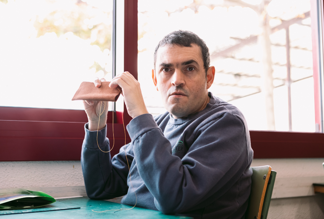 Una persona autistas sentada en una mesa, sostiene un objeto de cuero y mira a la cámara