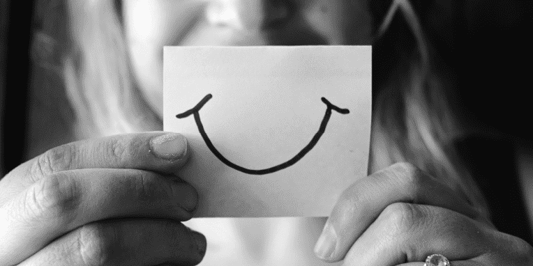 Un papel sujeto entre dos manos con una sonrisa dibujada