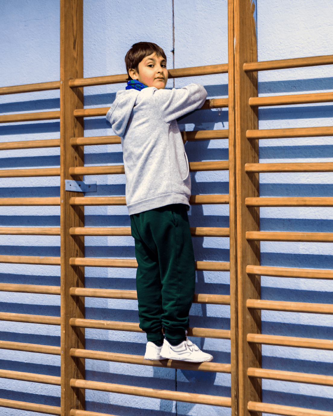 Niño subido a unas espalderas en un gimnasio de colegio.