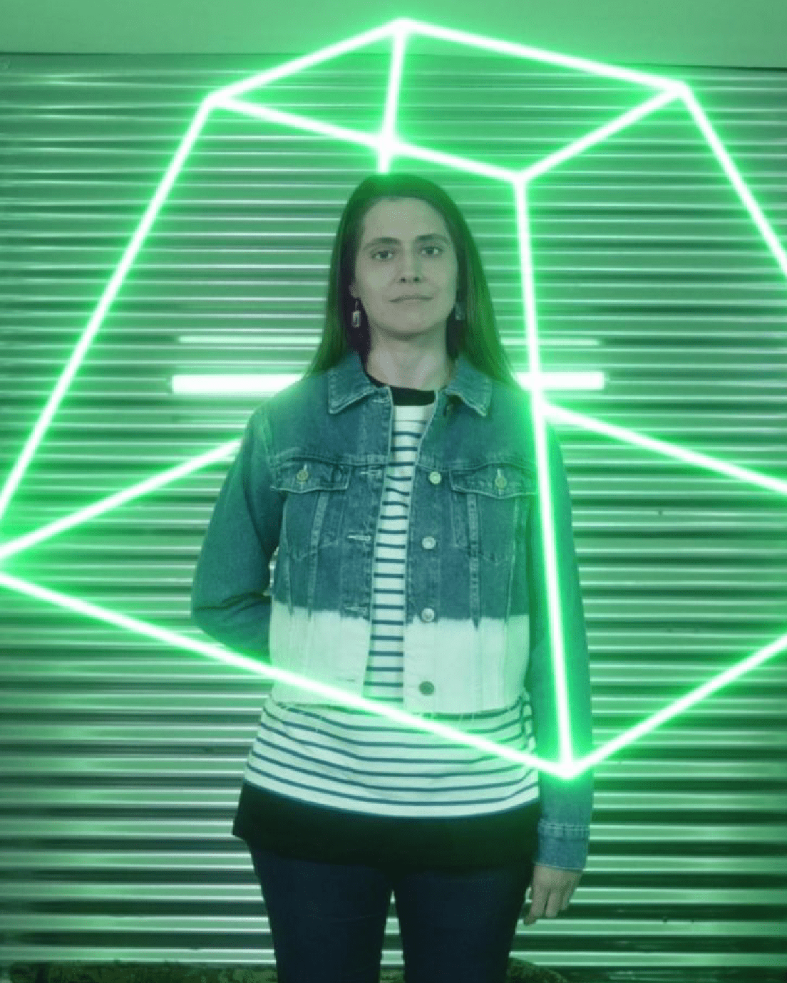 En la foto aparece una joven mirando al frente con luces de neon verde por detrás con formas aritmétricas