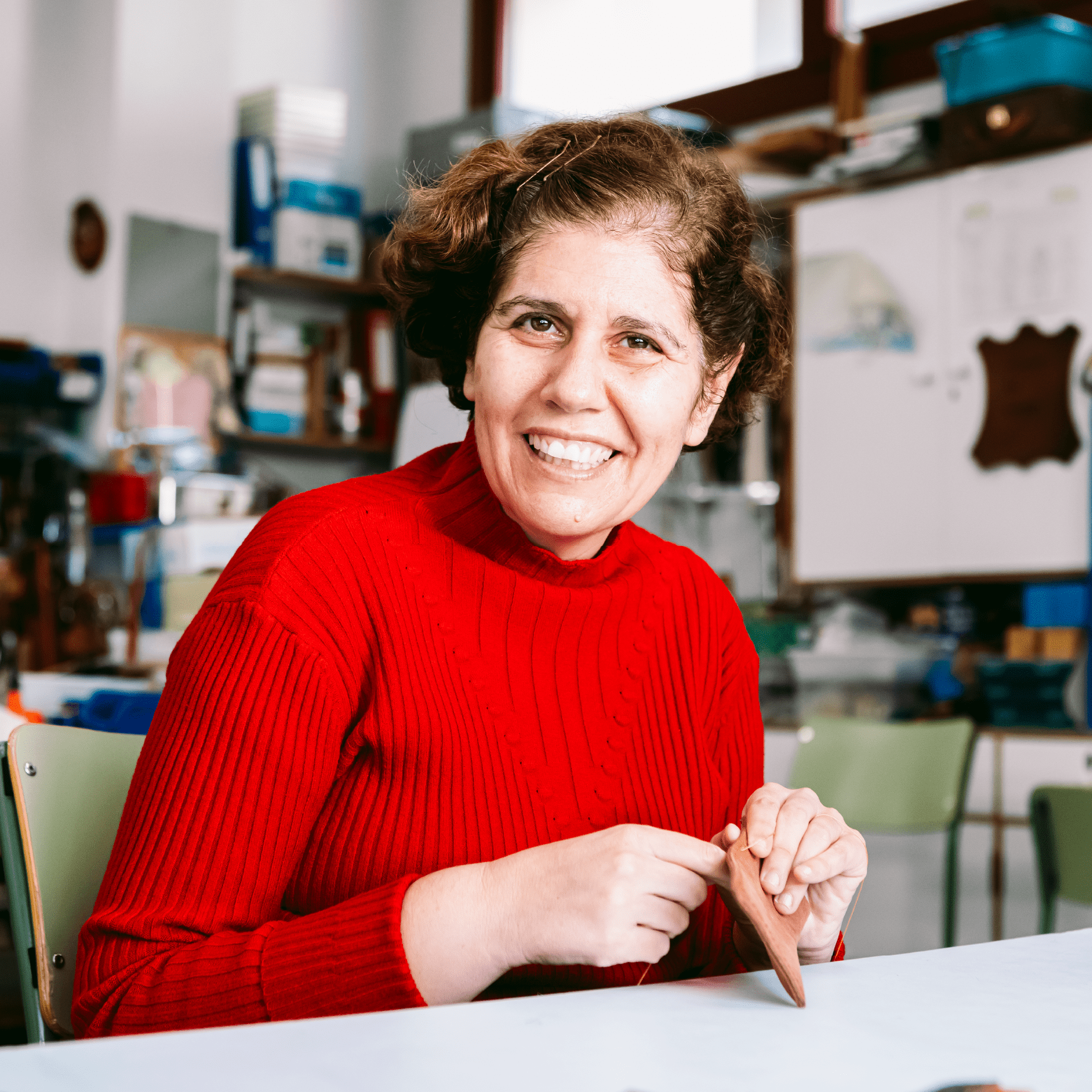 Una mujer sonriendo y mirando a la cámara mientras cose una pieza de cuero