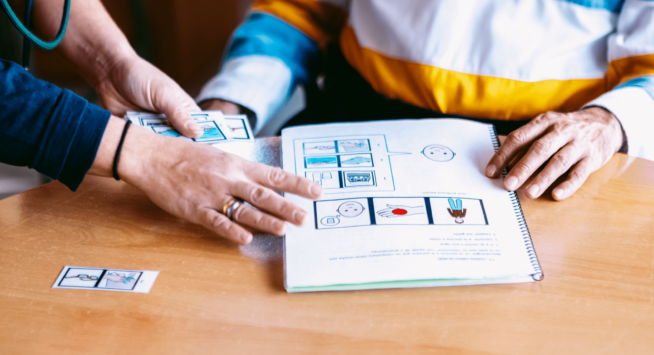 Se ven unas manos de mujer adulta y las d un niño sobre un libro con pictogramas