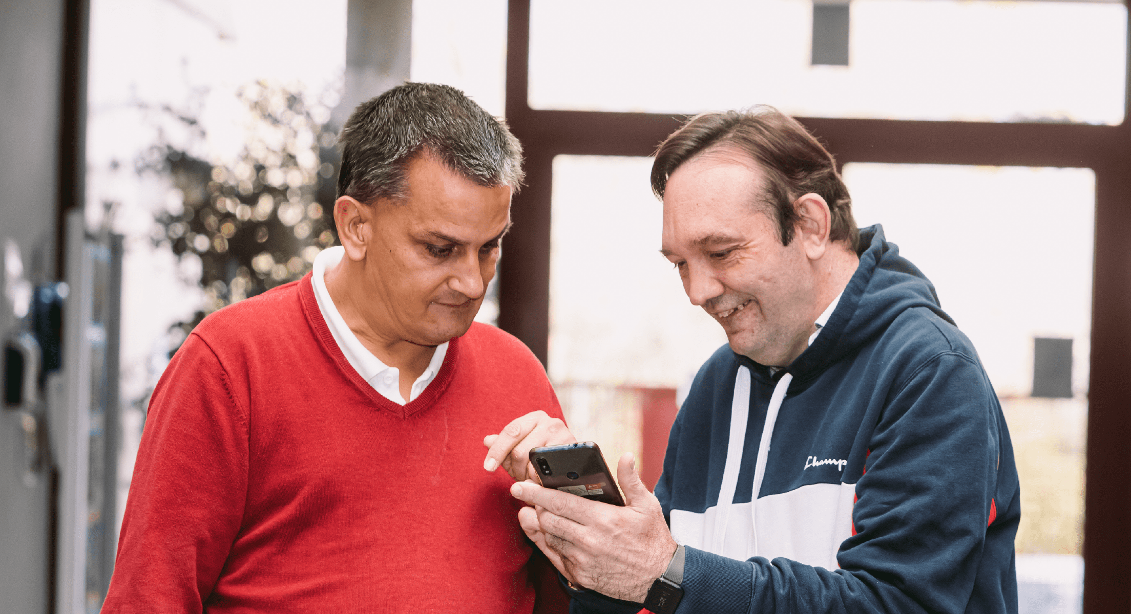Hombre adulto mostrando el teléfono a otro compañero con una sonrisa.