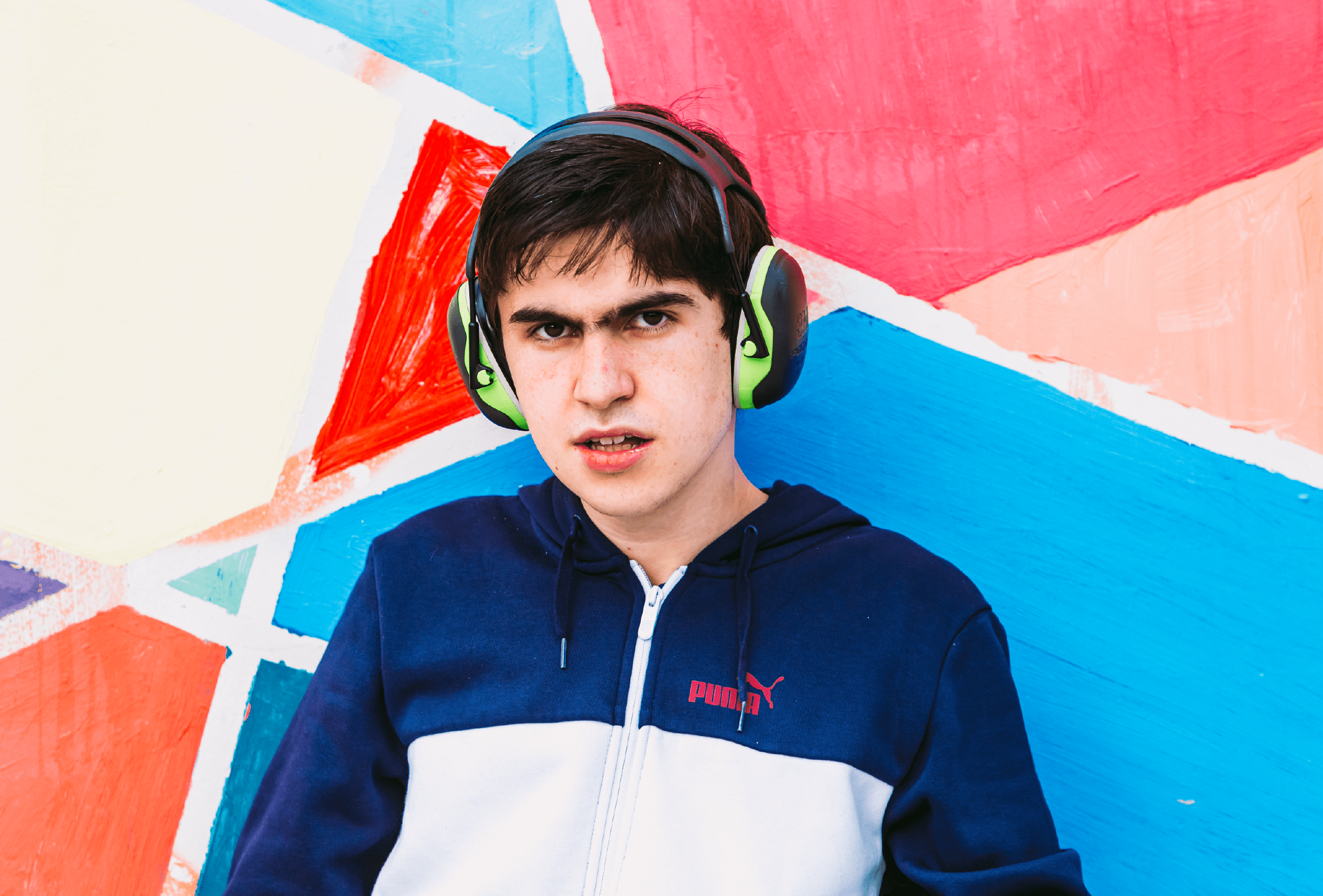 Chico con cascos antirruido mirando a cámara delante de un mural multicolor