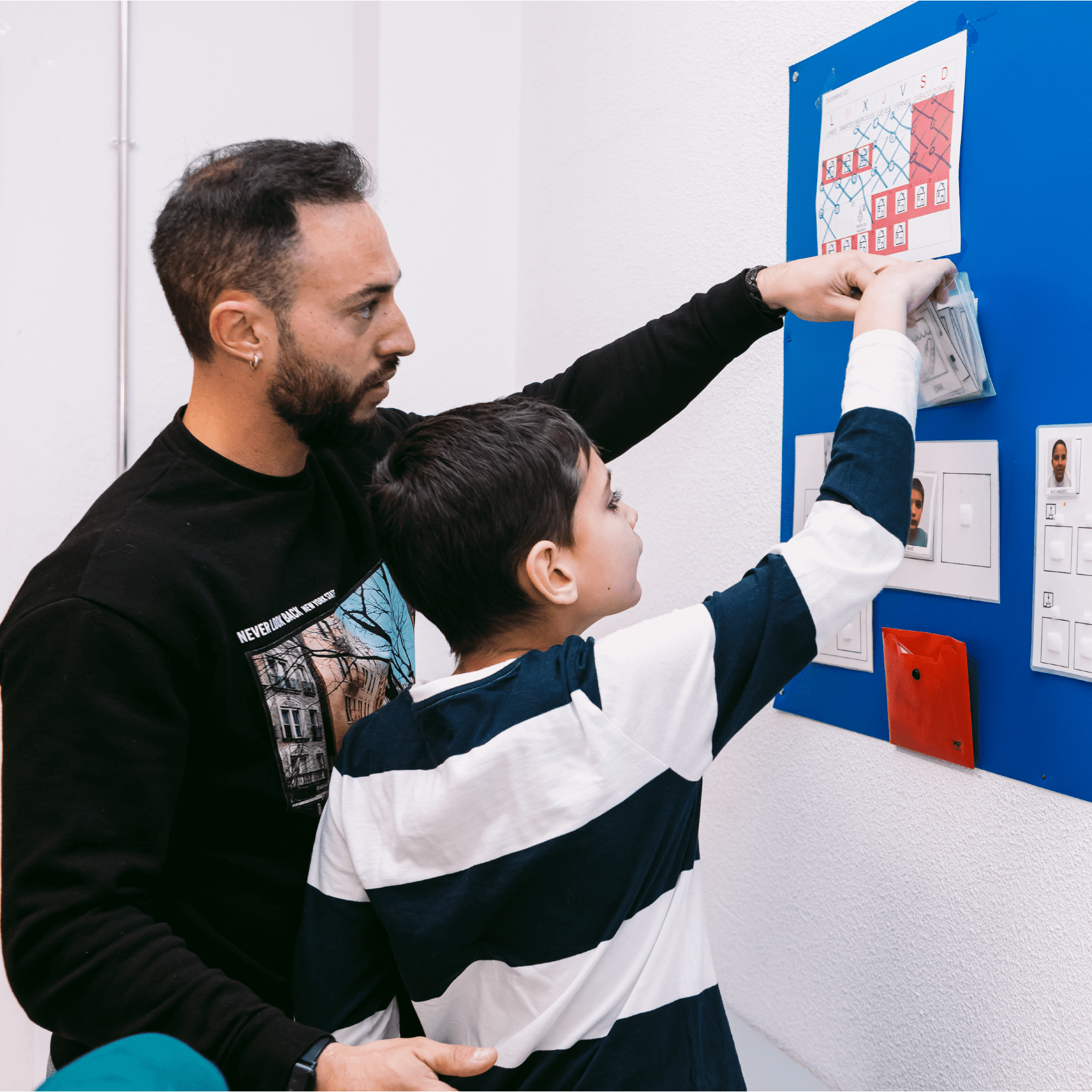 Un niño colocando un papel en una pizarra con la ayuda de su persona de apoyo