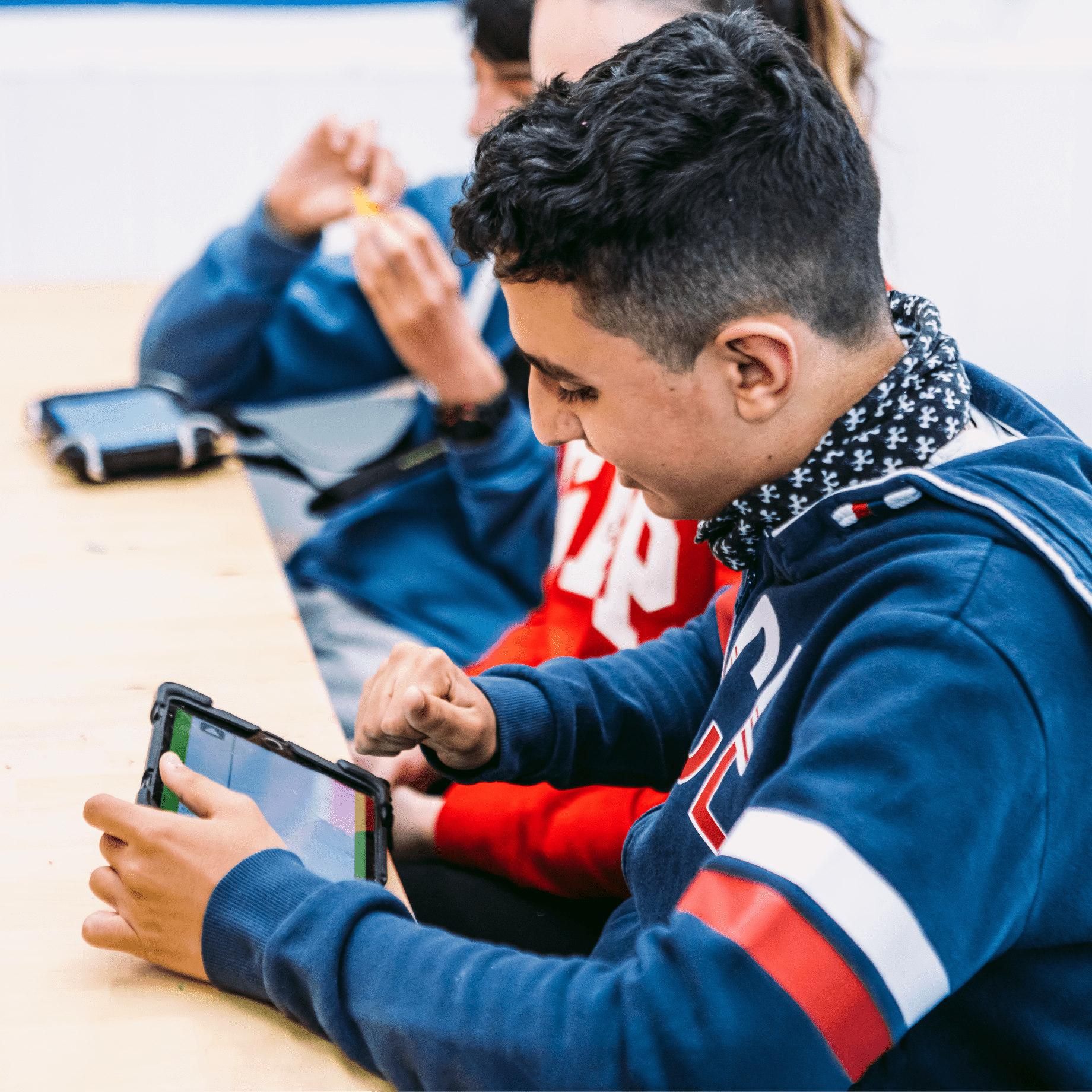 Chico joven sentado en un aula cogiendo una tablet, con compañeros al lado