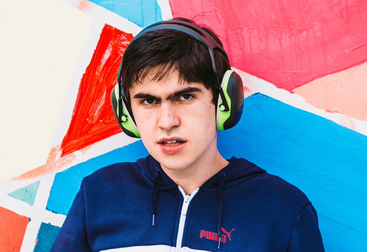 Chico con cascos antirruido mirando a cámara delante de un mural multicolor