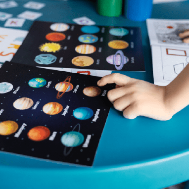 Mano de niño señalando una hoja con planetas.