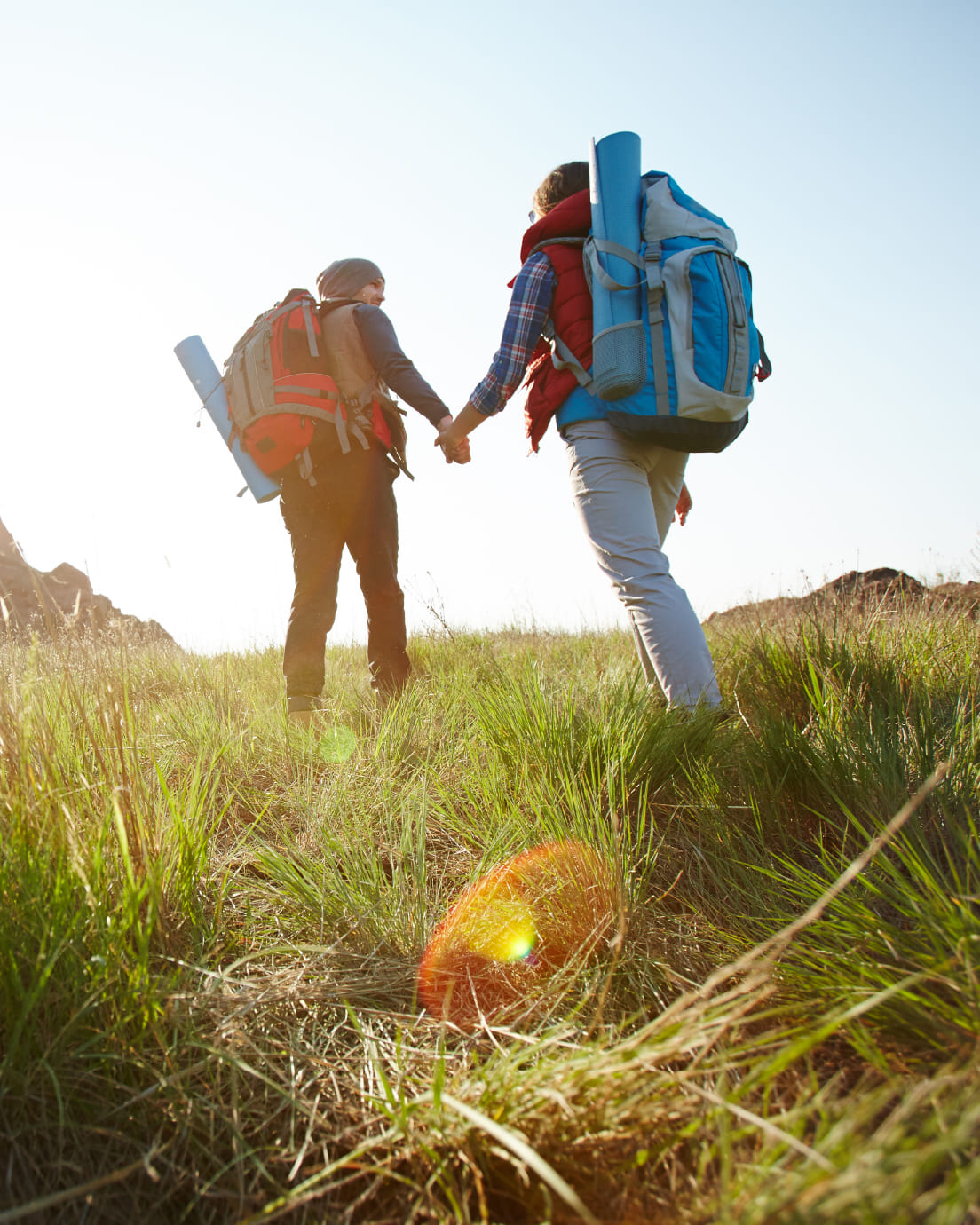 Dos personas mochileras cogidas de la mano caminando en un paisaje natural.
