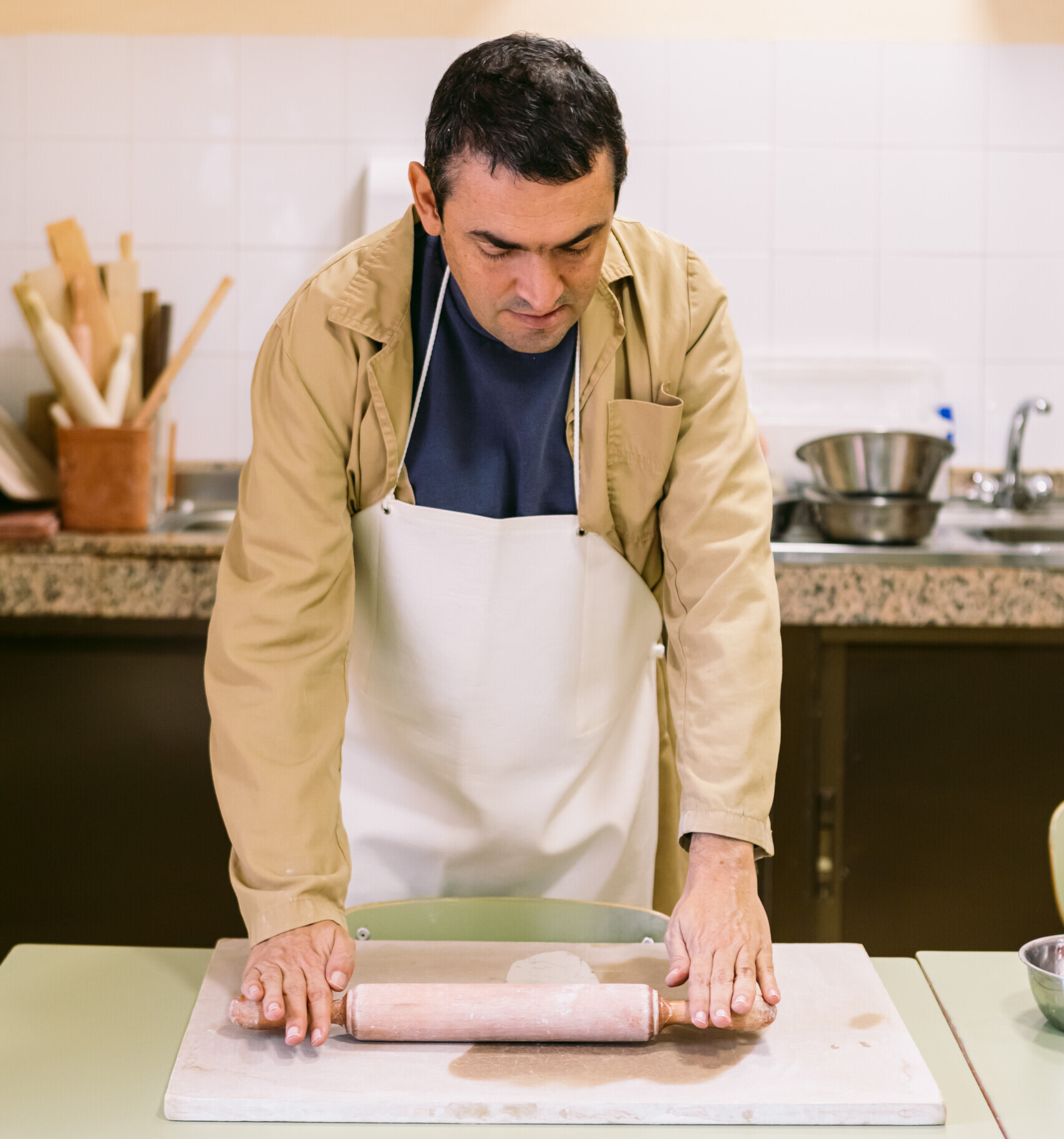 Hombre adulto con delantal trabajando con un rodillo amasador.
