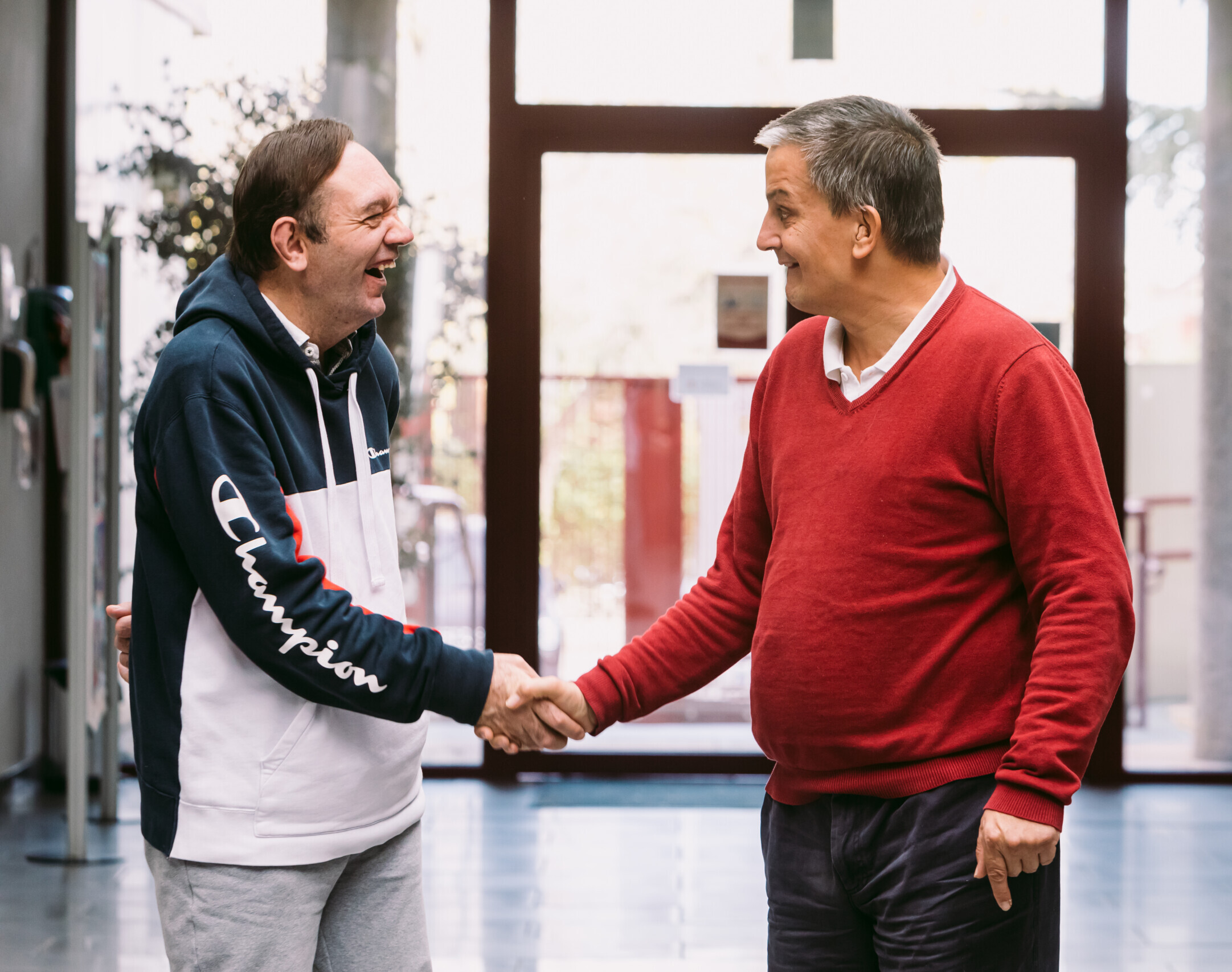 Dos hombres con autismo dándose la mano sonrientes