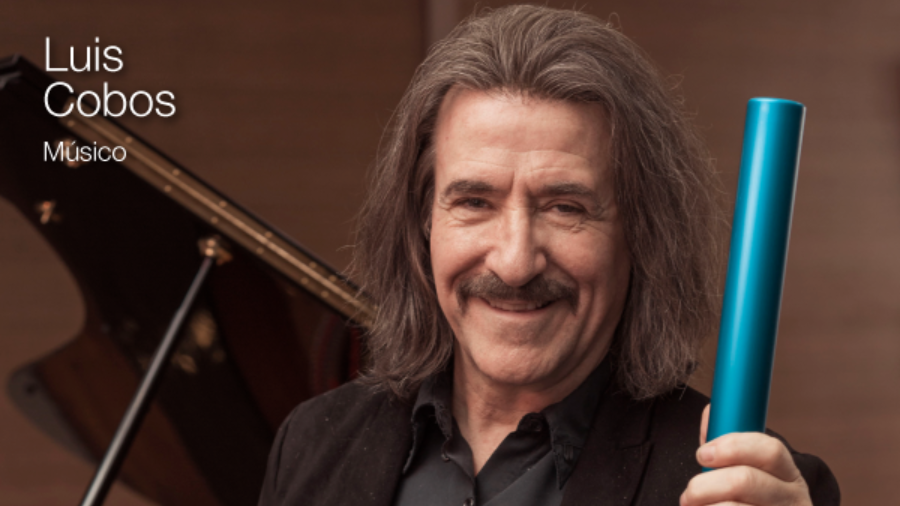 El músico Luis Cobos mirando a cámara sonriendo con un testigo azul en la mano