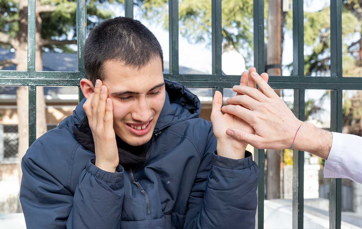 Un chico autista sonriendo y dándole la mano a otra persona