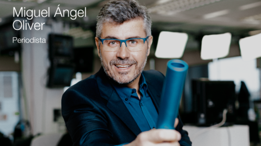 El periodista Miguel Angel Oliver sonriendo a cámara con un testigo azul en la mano