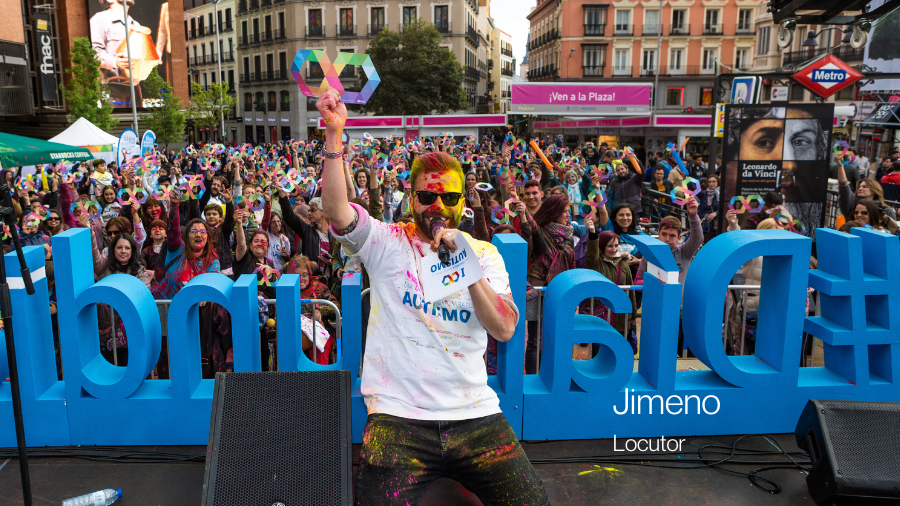 El presentador Jimeno mirando a cámara y posando con un infinito multicolor sobre un escenario