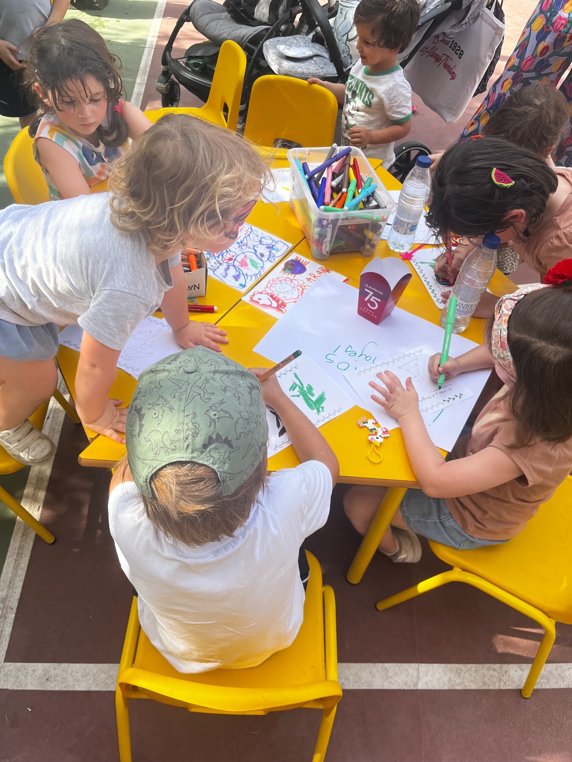 Un grupo de niños dibujando y pintando en folios sobre una mesa amarilla