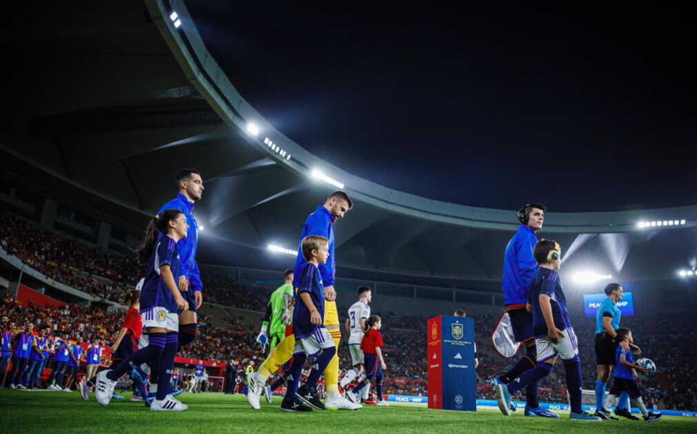 Tres jugadores de la sección masculina de fútbol junto a tres menores con autismo saliendo al campo de fútbol