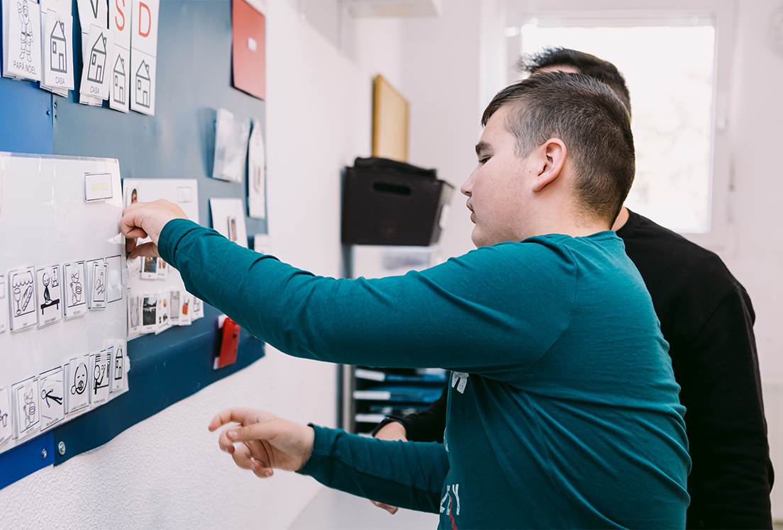 Un chico autista señalando un tablón con pictogramas