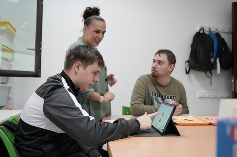 Dos chicos con autismo utilizando una tablet junto con su persona de apoyo