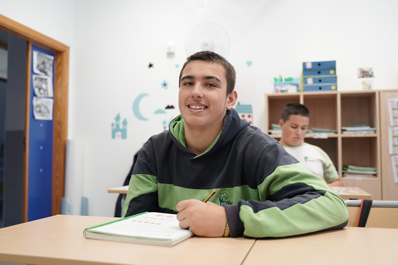 Un chico autista mirando a cámara sonriente escribiendo en un cuaderno