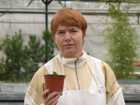 Una mujer autista mirando a cámara sujetando una maceta con una planta