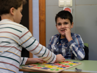 Un niño autista de espaldas jugando con otro niño con autismo que está mirando a cámara