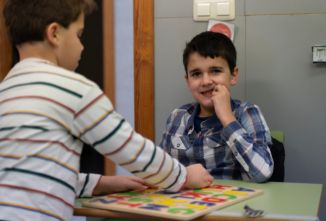 Un niño autista de espaldas jugando con otro niño con autismo que está mirando a cámara