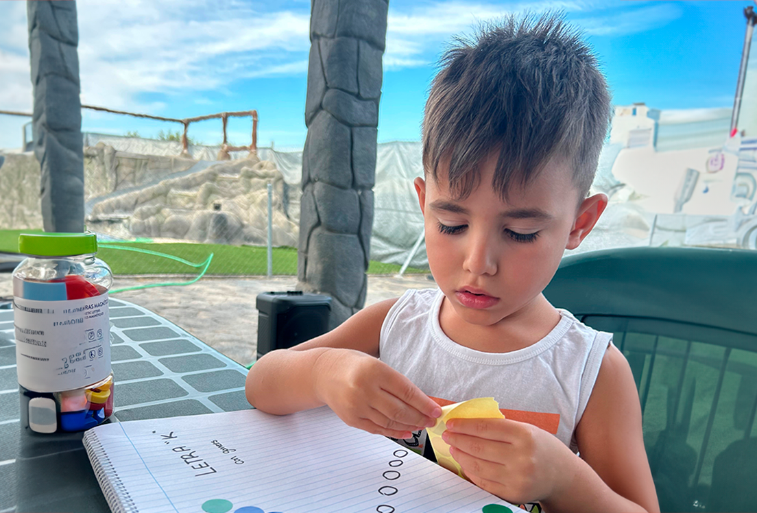 Fotografía de Kinillo, un niño autista, aprendiendo la letra K en un cuaderno con pegatinas