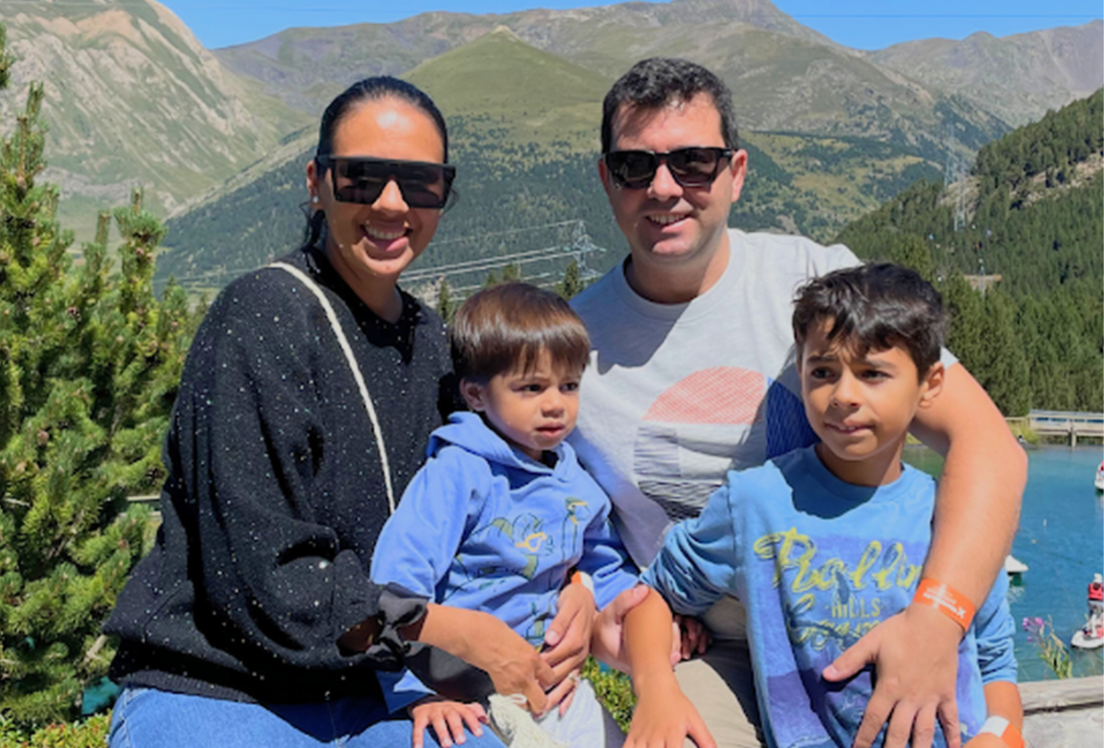 Una mujer y un hombre con gafas de sol sonríen a cámara abrazados cada uno a un niño