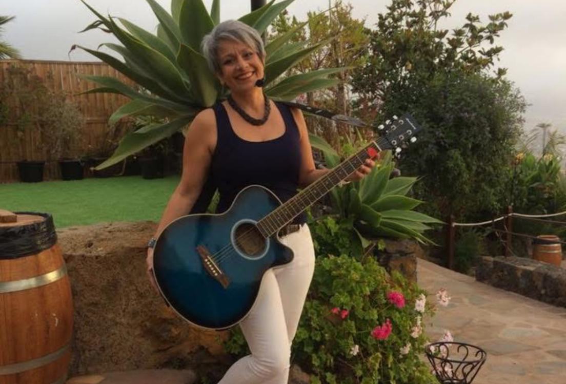 Una mujer sujeta una guitarra y mira a la cámara en un jardín